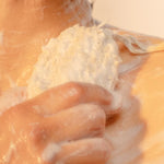 Hands using ORGANIC TERRA CO.®natural sisal soap exfoliating pouch to lather botanical soap bar on skin under shower water