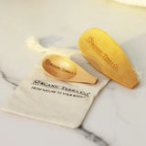 ORGANIC TERRA CO.® engraved wooden spoon and wooden spatula on branded cotton muslin pouch displaying From Nature To Your Body trademark on marble surface