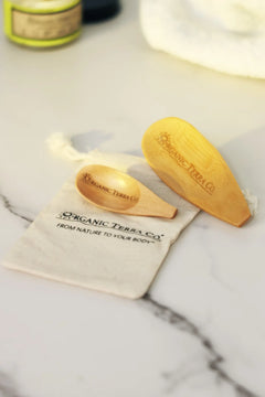 ORGANIC TERRA CO.® engraved wooden spoon and wooden spatula on branded cotton muslin pouch displaying From Nature To Your Body trademark on marble surface