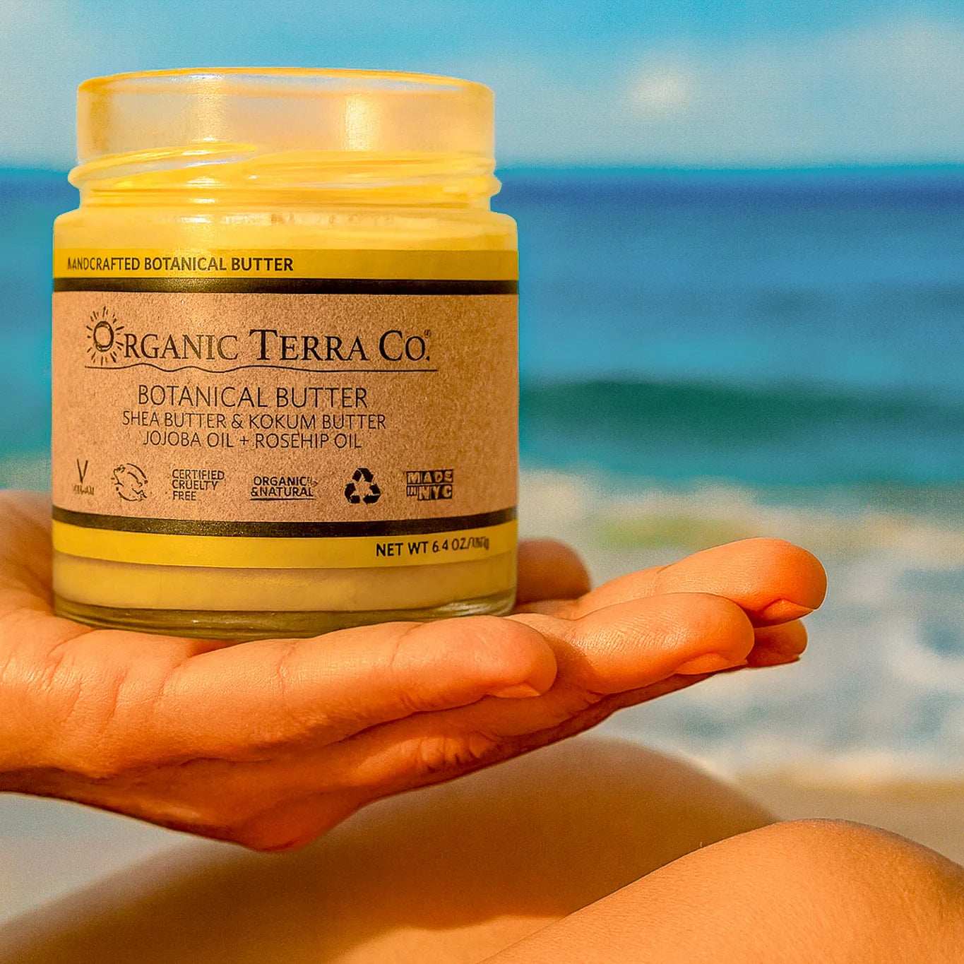 ORGANIC TERRA CO.® Butter jar with shea butter kokum butter jojoba and rosehip oil held by hand at beach