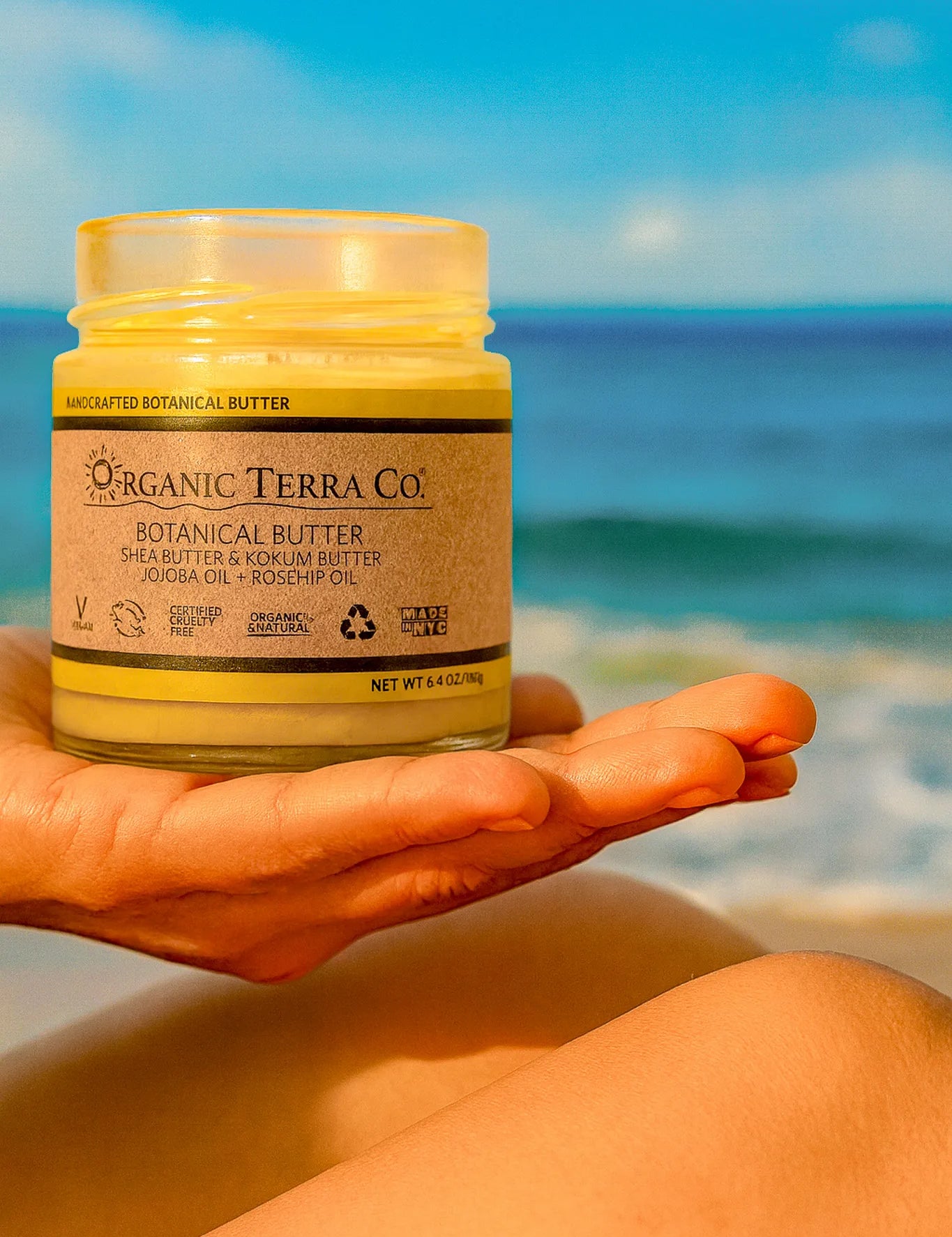 ORGANIC TERRA CO.® Butter jar with shea butter kokum butter jojoba and rosehip oil held by hand at beach