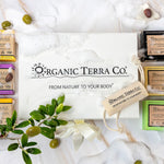 Organic Terra Co. Botanical Cleansing Collection gift set displayed on white marble with six artisan soap bars, olive branches, and soap suds.