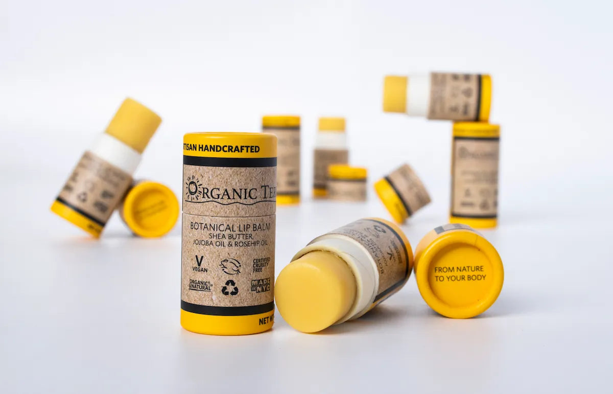  Multiple ORGANIC TERRA CO.® Botanical Lip Balm tubes with shea butter jojoba oil and rosehip oil scattered on white background showing From Nature To Your Body trademark
