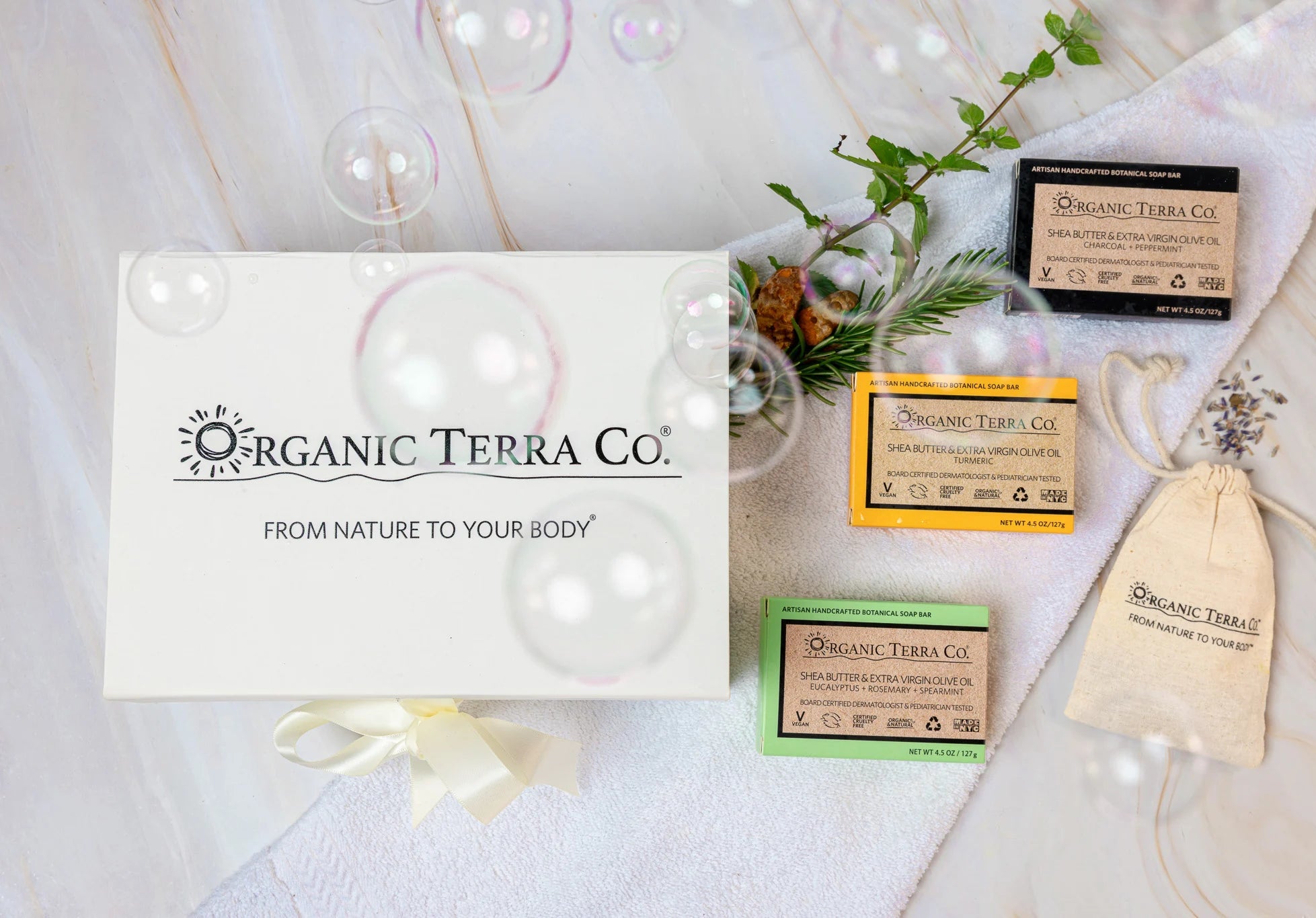 Organic Terra Co. Botanical Cleansing Trio — white gift box with ribbon and three handcrafted botanical soap bars on a soft towel