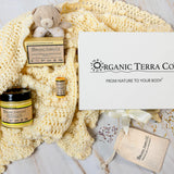 Organic Terra Co. Mama & Baby Collection — gift box with unscented botanical soap, Botanical Butter, lip balm and lavender pouch on a soft cream baby blanket with teddy bear