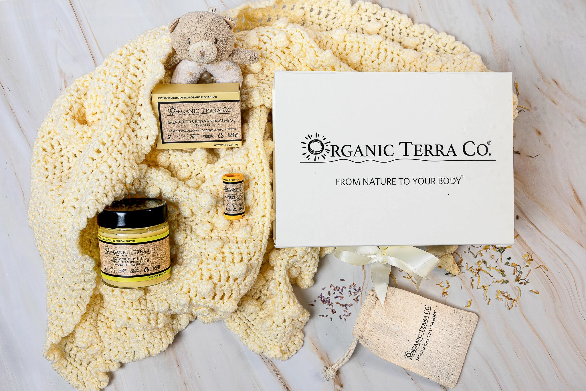 Organic Terra Co. Mama & Baby Collection — gift box with unscented botanical soap, Botanical Butter, lip balm and lavender pouch on a soft cream baby blanket with teddy bear