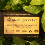 ORGANIC TERRA CO.® Butter Extra Virgin Olive Oil Charcoal and Peppermint soap bar box resting on wet fresh peppermint leaves