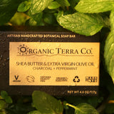 ORGANIC TERRA CO.® Butter Extra Virgin Olive Oil Charcoal and Peppermint soap bar box resting on wet fresh peppermint leaves