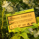 ORGANIC TERRA CO.® Butter Extra Virgin Olive Oil Eucalyptus Rosemary and Spearmint soap bar box resting on wet fresh eucalyptus rosemary and spearmint leaves
