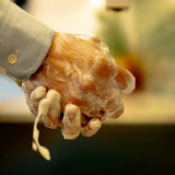 Hands lathering ORGANIC TERRA CO.®botanical soap bar producing rich creamy foam with water dripping