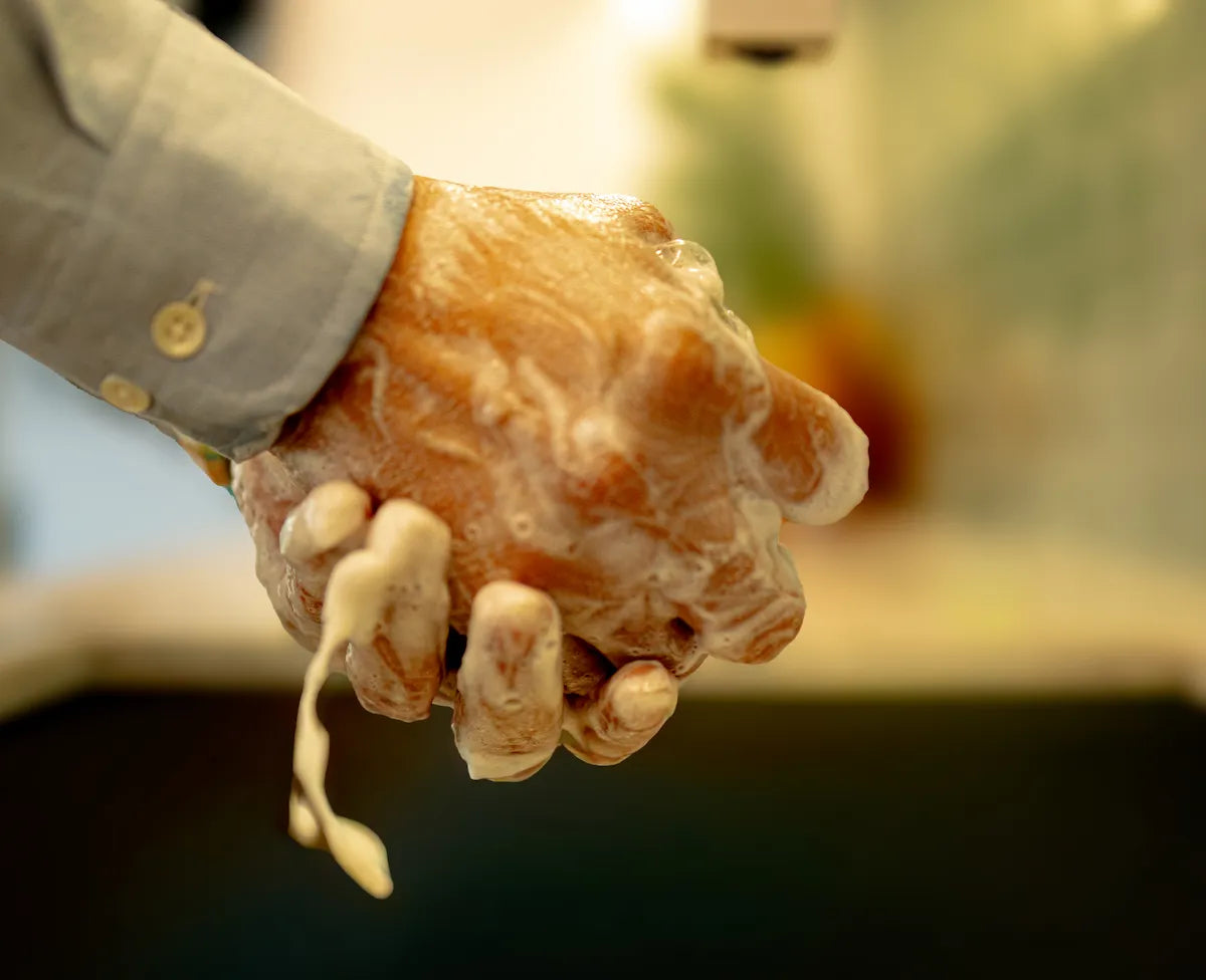 Hands lathering ORGANIC TERRA CO.®botanical soap bar producing rich creamy foam with water dripping
