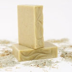 Two ORGANIC TERRA CO.®handcrafted Shea Butter Extra Virgin Olive Oil Eucalyptus Rosemary and Spearmint soap bars stacked surrounded by french green clay powder and dried herbs on white background