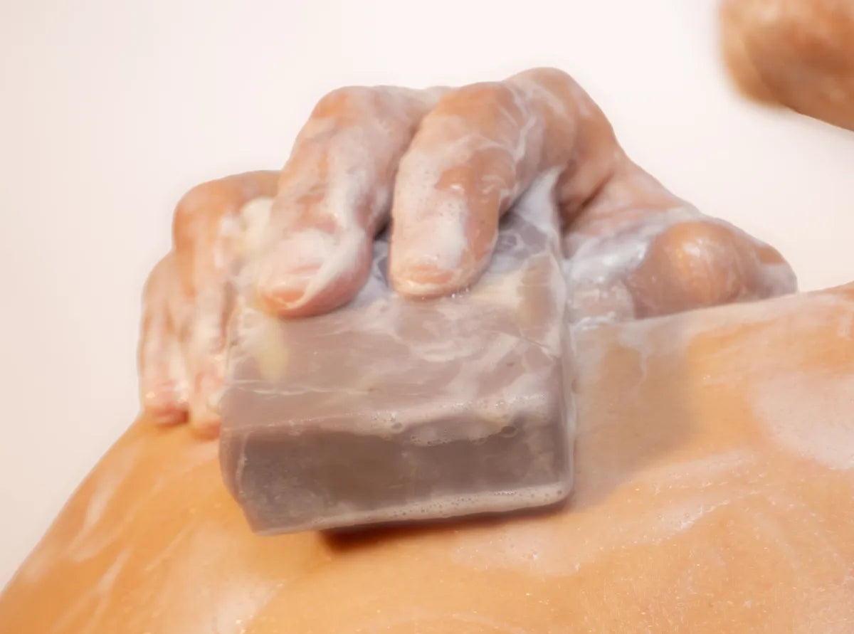 Hand lathering ORGANIC TERRA CO.® Lavender botanical soap bar on wet skin under shower water
