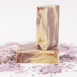 ORGANIC TERRA CO.®handcrafted Shea Butter Extra Virgin Olive Oil Lavender soap bars stacked surrounded by lavender powder and dried lavender buds on white background