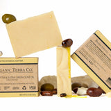 ORGANIC TERRA CO,© Butter and Extra Virgin Olive Oil unscented soap bar showing front and back packaging with fair trade ingredients alongside unwrapped bar and shea nuts