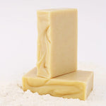 Two ORGANIC TERRA CO.® Shea Butter and Extra Virgin Olive Oil unscented soap bars stacked on arrowroot powder on white background