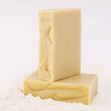 Two ORGANIC TERRA CO.® Shea Butter and Extra Virgin Olive Oil unscented soap bars stacked on arrowroot powder on white background