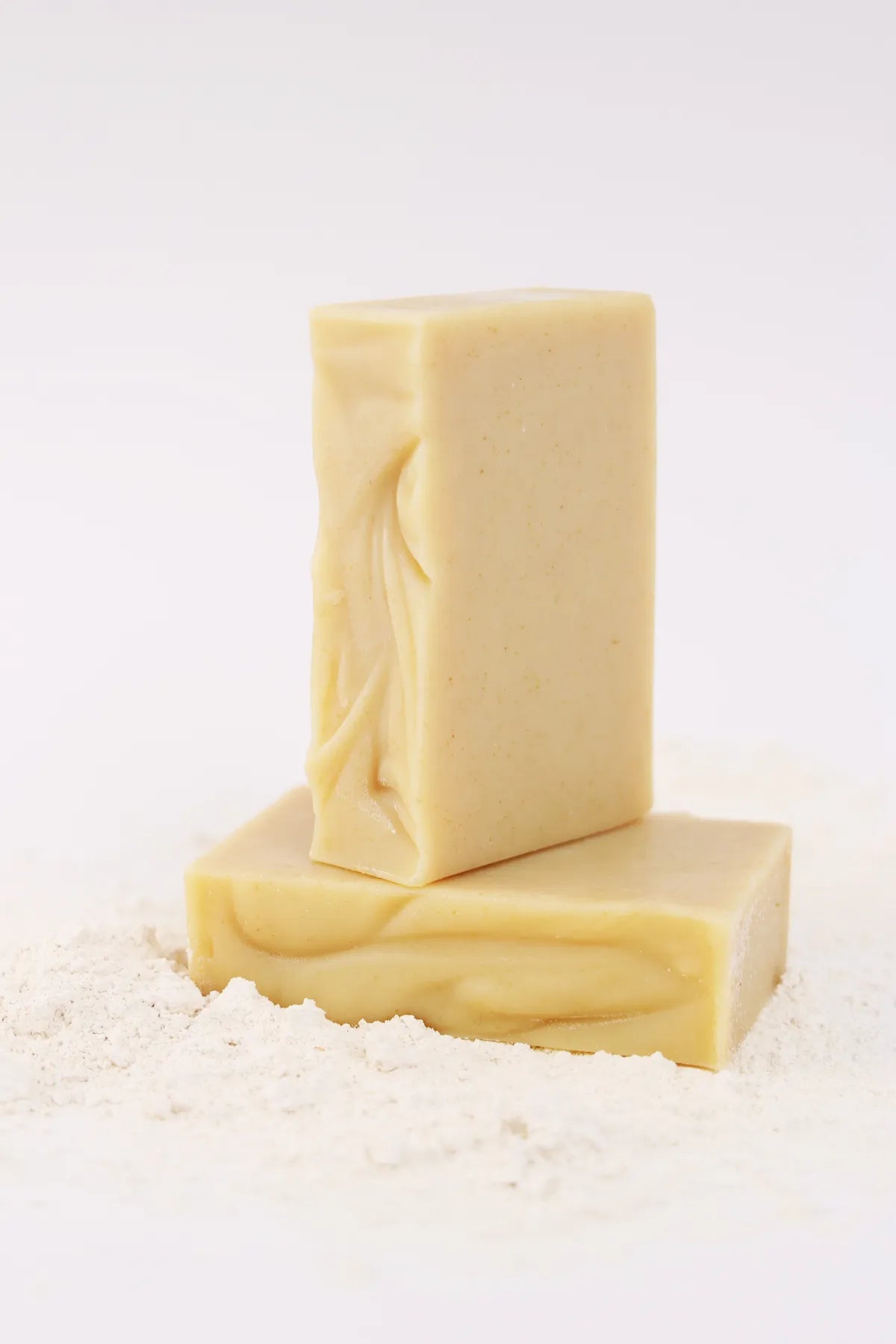 Two ORGANIC TERRA CO.® Shea Butter and Extra Virgin Olive Oil unscented soap bars stacked on arrowroot powder on white background
