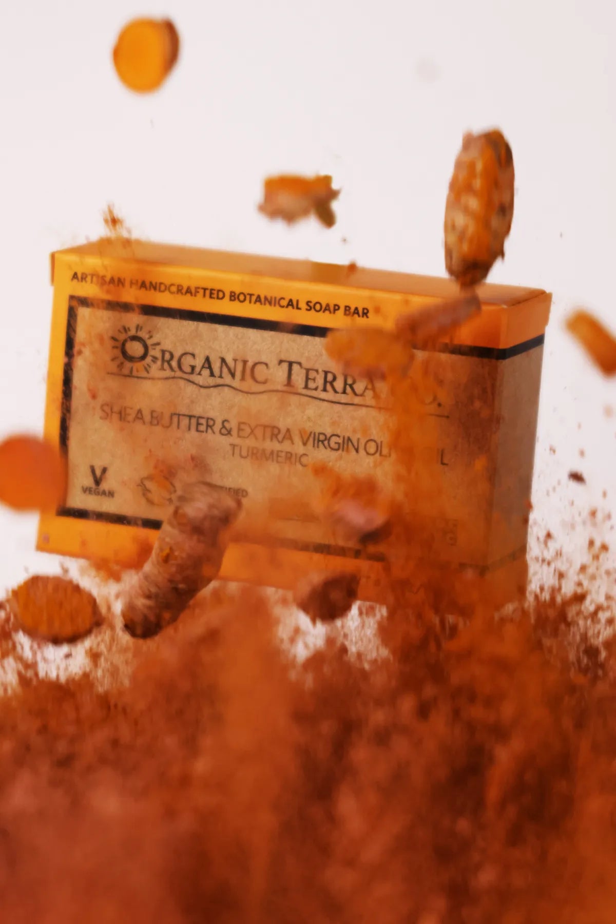 ORGANIC TERRA CO.®Shea Butter Extra Virgin Olive Oil Turmeric soap bar box emerging dramatically from turmeric powder cloud with fresh turmeric root pieces