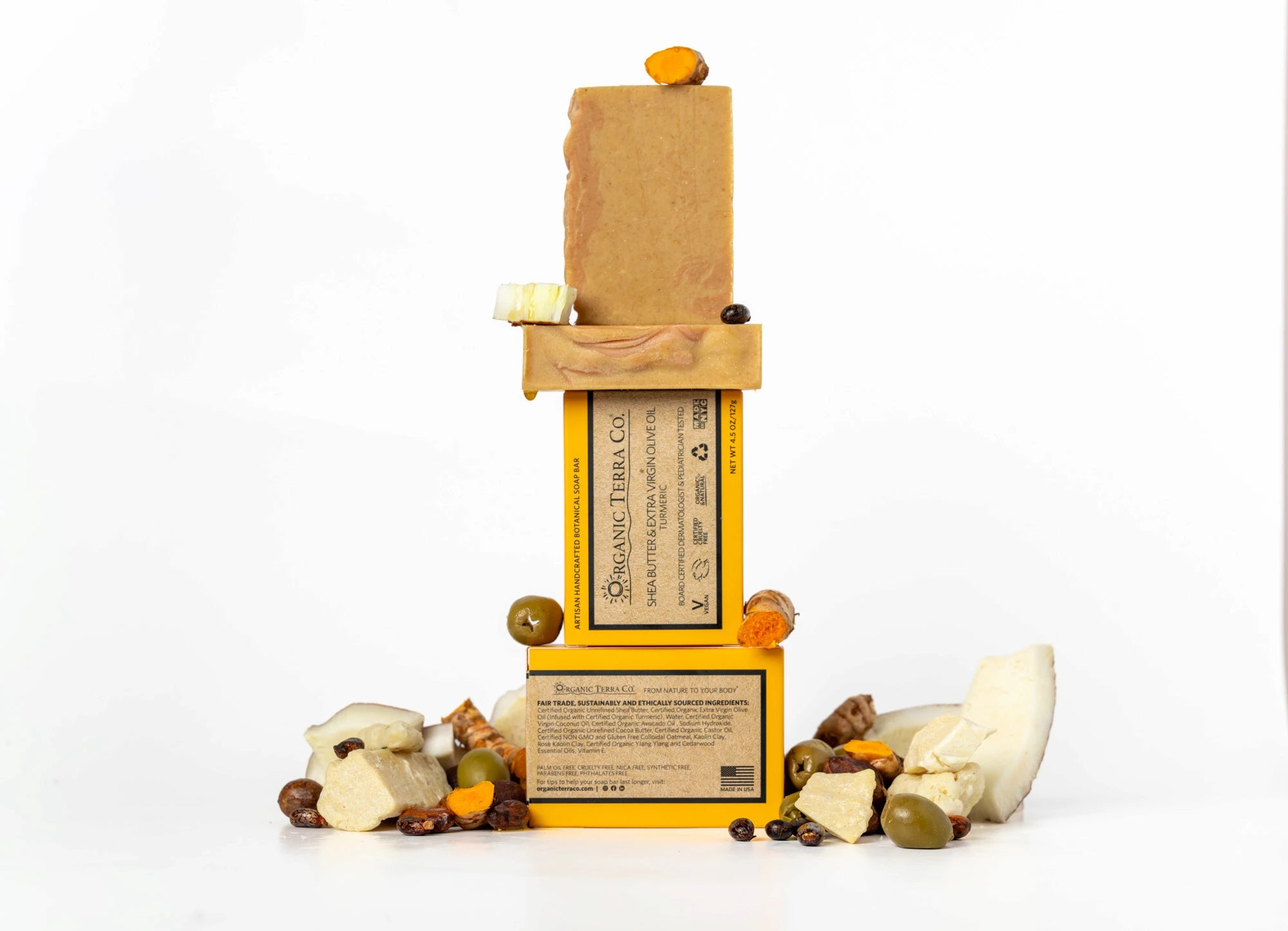 ORGANIC TERRA CO.® Extra Virgin Olive Oil Turmeric soap bar front and back packaging stacked with unwrapped bars and scattered turmeric root olives shea nuts and coconut