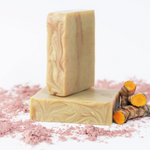 ORGANIC TERRA CO.®handcrafted Shea Butter Extra Virgin Olive Oil Turmeric soap bars stacked with fresh turmeric root and pink clay powder on white background