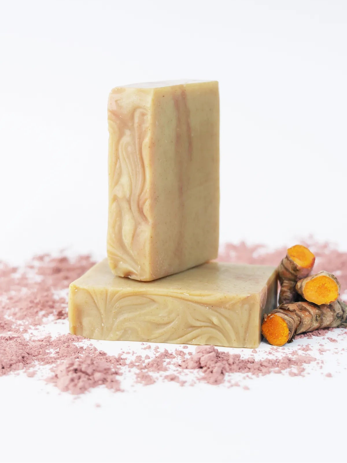 ORGANIC TERRA CO.®handcrafted Shea Butter Extra Virgin Olive Oil Turmeric soap bars stacked with fresh turmeric root and pink clay powder on white background