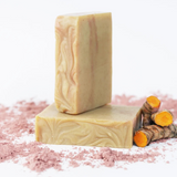 ORGANIC TERRA CO.®handcrafted Shea Butter Extra Virgin Olive Oil Turmeric soap bars stacked with fresh turmeric root and pink clay powder on white background
